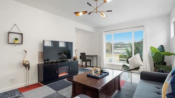 Una sala de estar moderna con televisor de pantalla plana, chimenea, mesa de centro, sofá y un amplio ventanal con vistas a la ciudad.