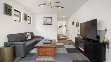 A modern living room with a grey sofa, wooden coffee table, and a black entertainment unit with a flat-screen TV.