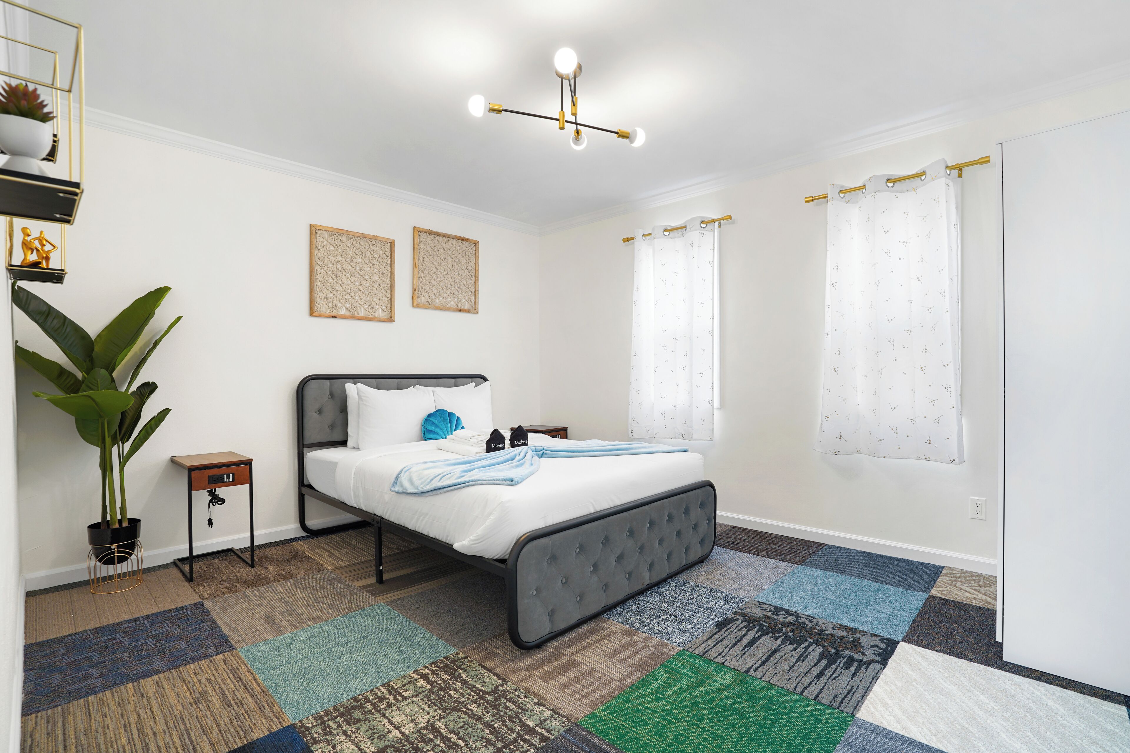 A bedroom with a bed, a nightstand, a potted plant, a wall-mounted shelf, and a ceiling light fixture.