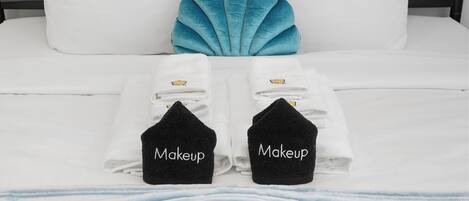 A neatly made bed with a blue decorative pillow, two towels labeled 'Makeup', and a blue patterned blanket.