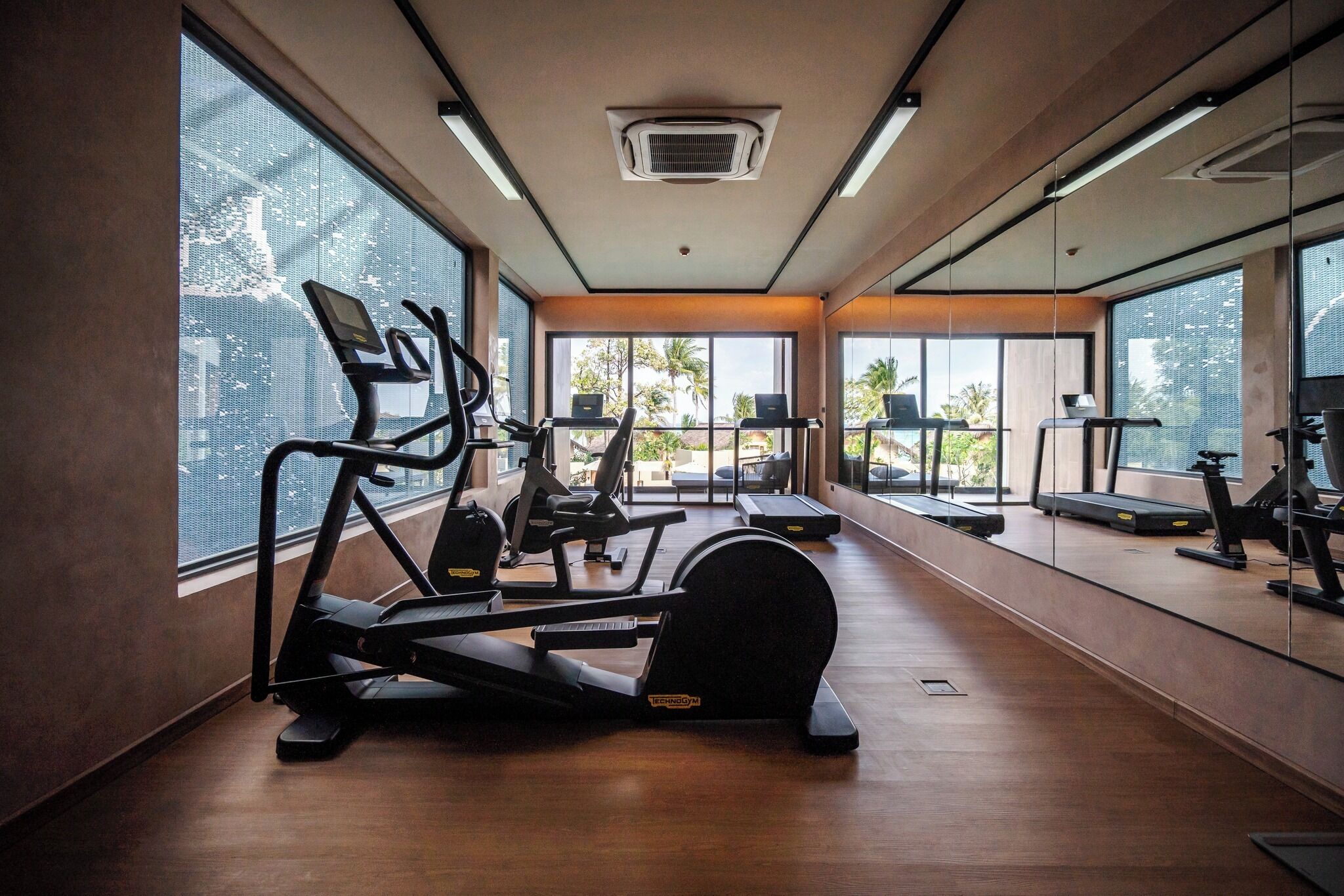Ein Fitnessstudio mit Laufbändern, Crosstrainern und einer Spiegelwand.