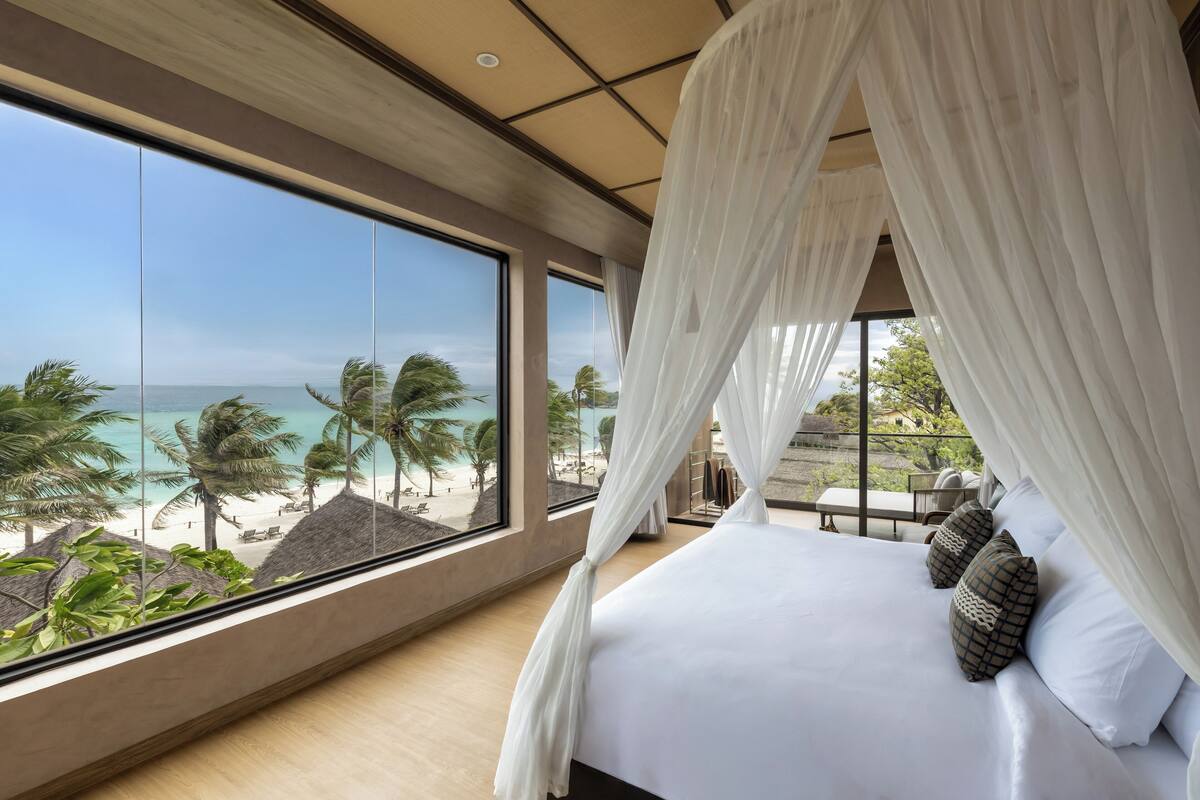A bedroom with a large window, a bed, and a view of the beach.