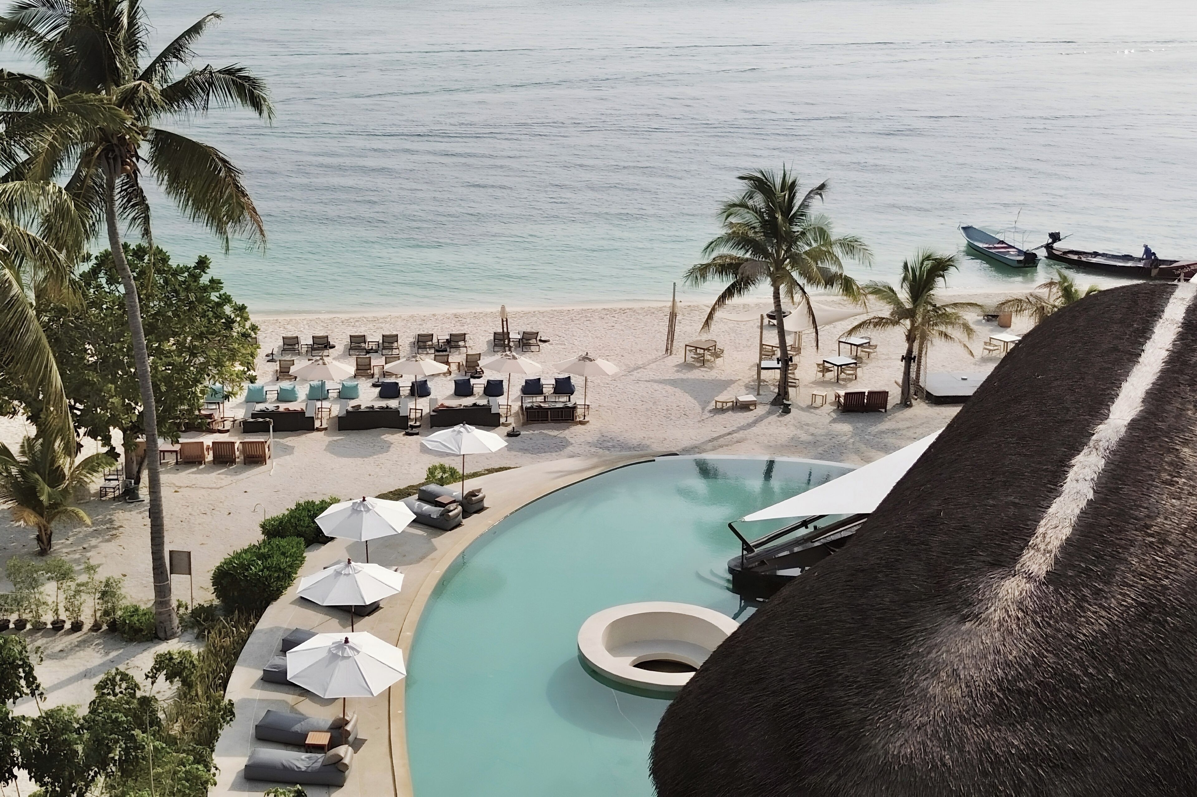 A resort with a pool, beach chairs, umbrellas, and palm trees.