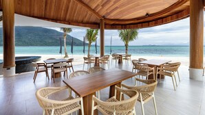An outdoor dining area with wooden tables and wicker chairs, overlooking a beach and ocean. - Irene Resort Koh Lipe (Koh Lipe)