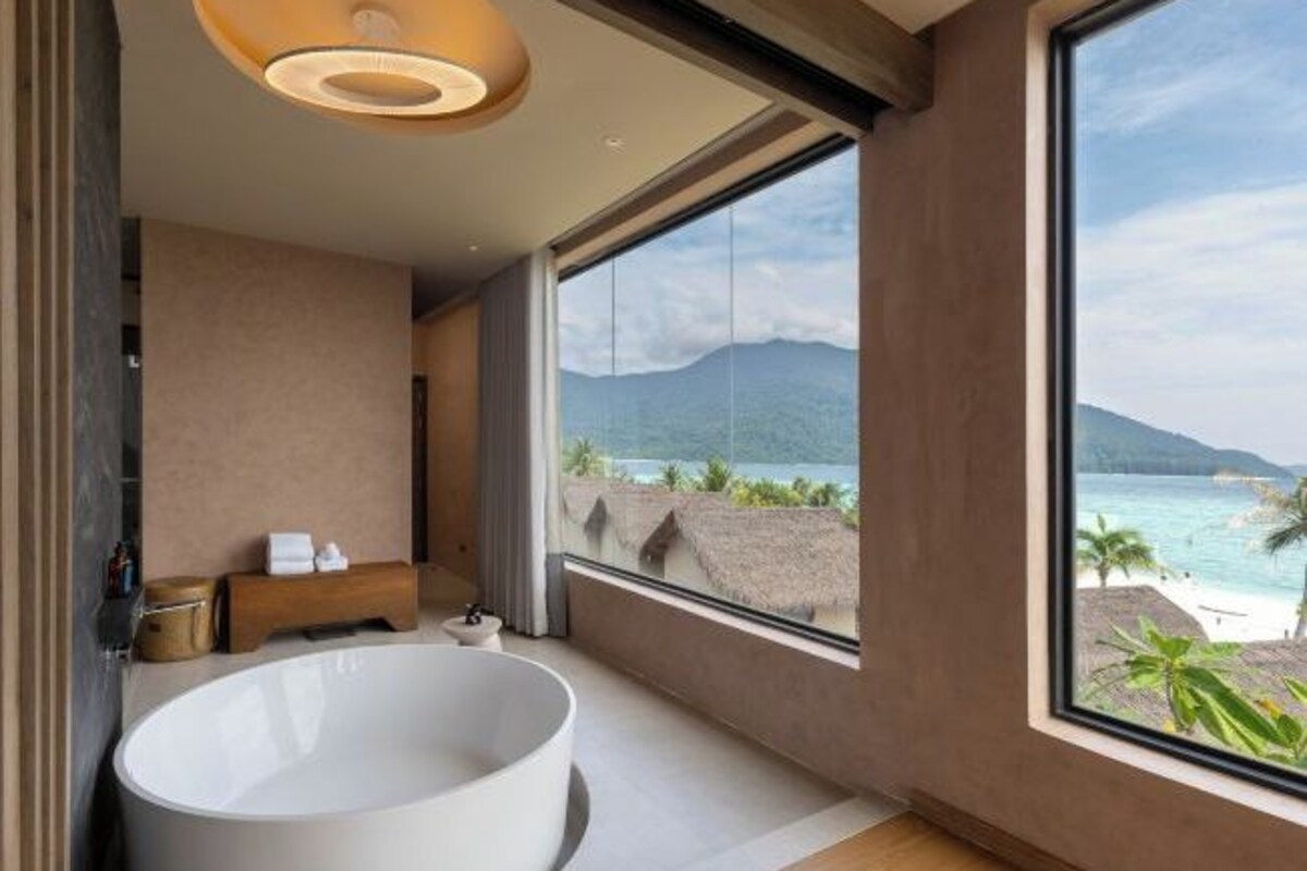 A modern bathroom with a large bathtub, a wooden bench, and a view of the ocean.