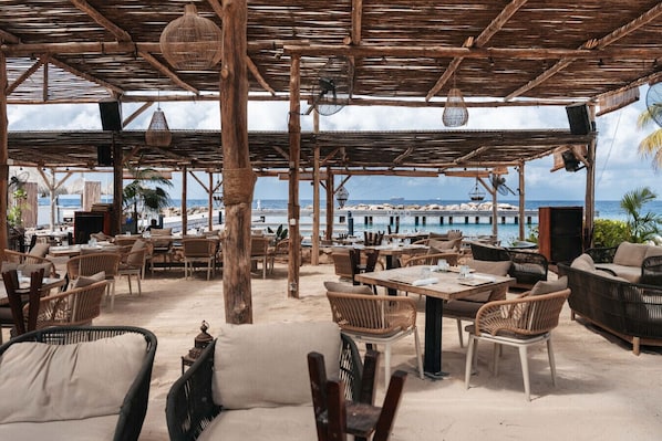 Un espace extérieur aménagé avec des meubles en osier, un plafond en bois et une vue sur la plage et l’océan.