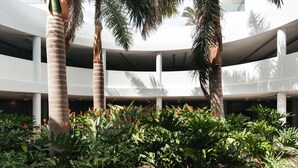 A modern building with a circular atrium, palm trees, and lush greenery.