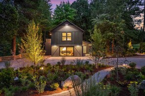Ein zweistöckiges Holzhaus mit einer großen Veranda, umgeben von einem angelegten Garten mit verschiedenen Pflanzen und einem Weg zum Eingang.
