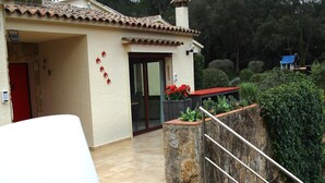 A house with a tiled roof, a red door, and a stone wall with a metal railing.