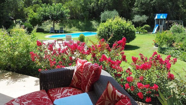 A patio area with a wicker sofa and cushions, a pool, and a slide in the background.