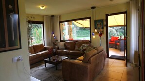 A living room with a sofa set, a coffee table, and a view of the garden through large windows.