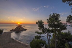 A coastal landscape with a sunset, a rocky outcrop, and a beach.