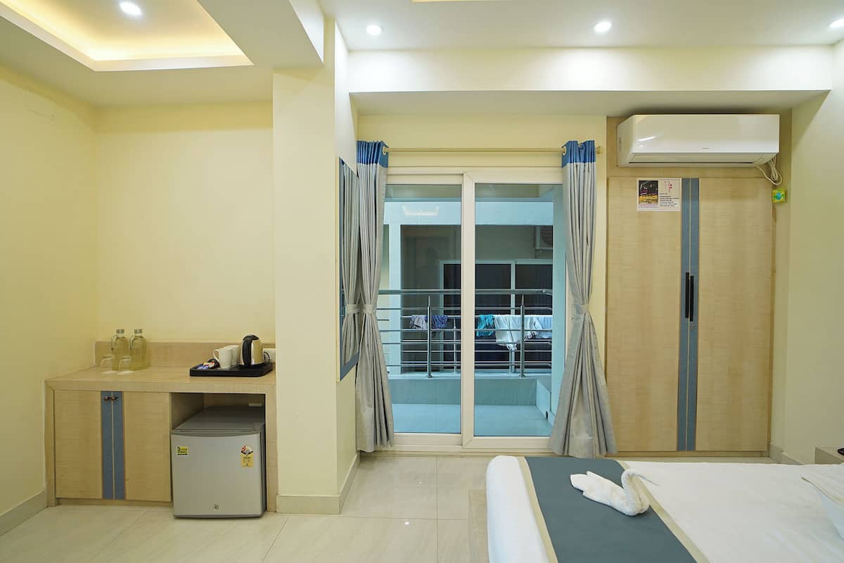 Habitación de hotel con cama, un pequeño escritorio con refrigerador, armario y puerta de vidrio corrediza que da a un balcón.