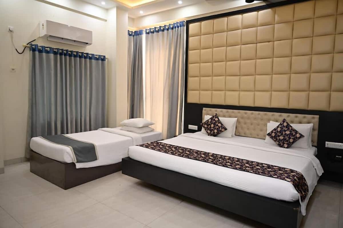 Habitación de hotel con una cama grande, una cama más pequeña, un sofá cama, un cabecero con diseño capitonado y un equipo de aire acondicionado.