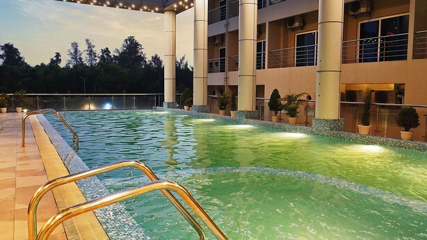 Una piscina con borde de azulejos, pasamanos metálico y un edificio con varios balcones al fondo.