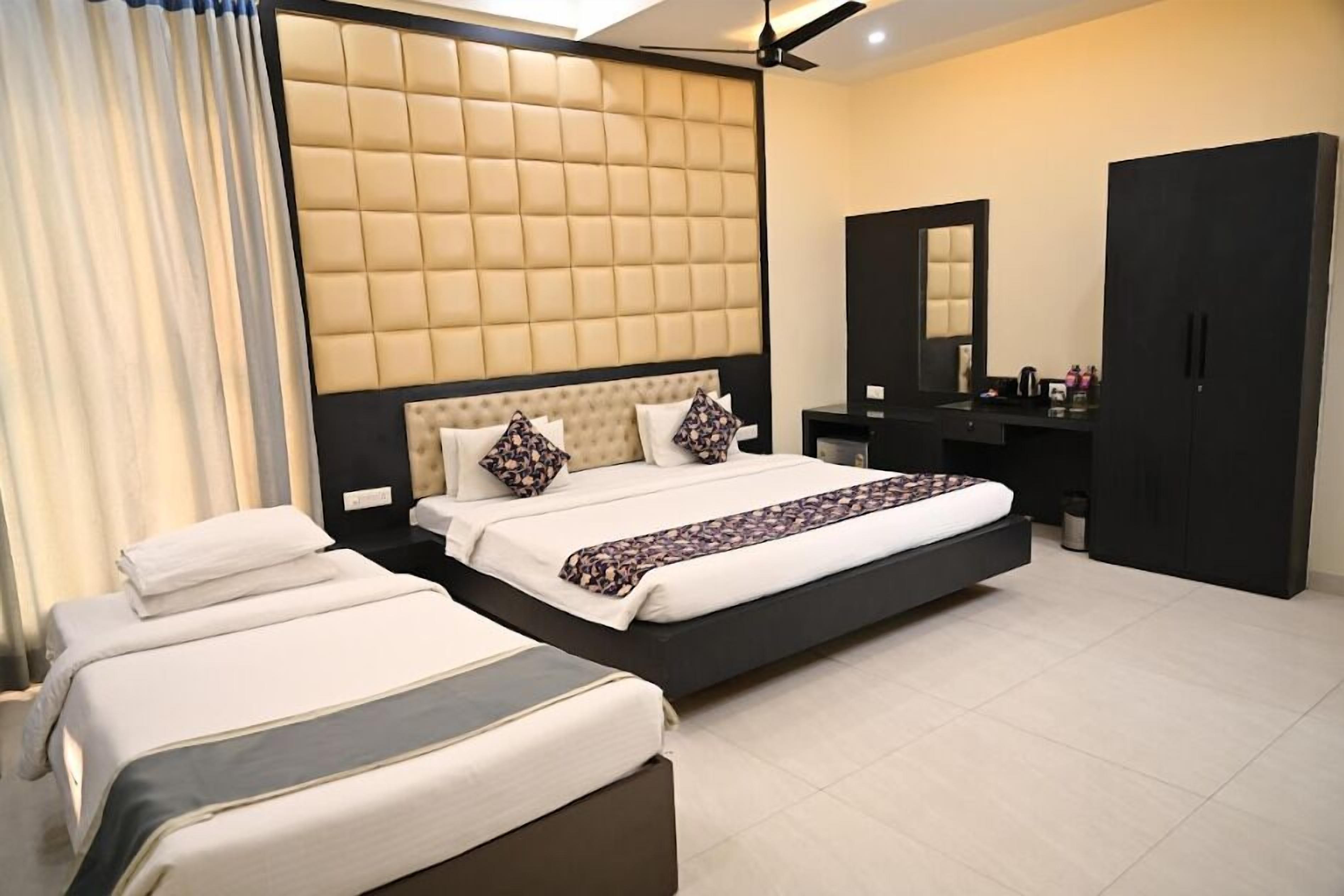 A modern hotel room with a large bed, a smaller bed, a vanity with a mirror, and a wardrobe.