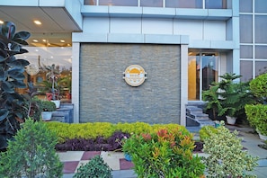 Un edificio con fachada de piedra, un logotipo en la pared y varios maceteros en primer plano.