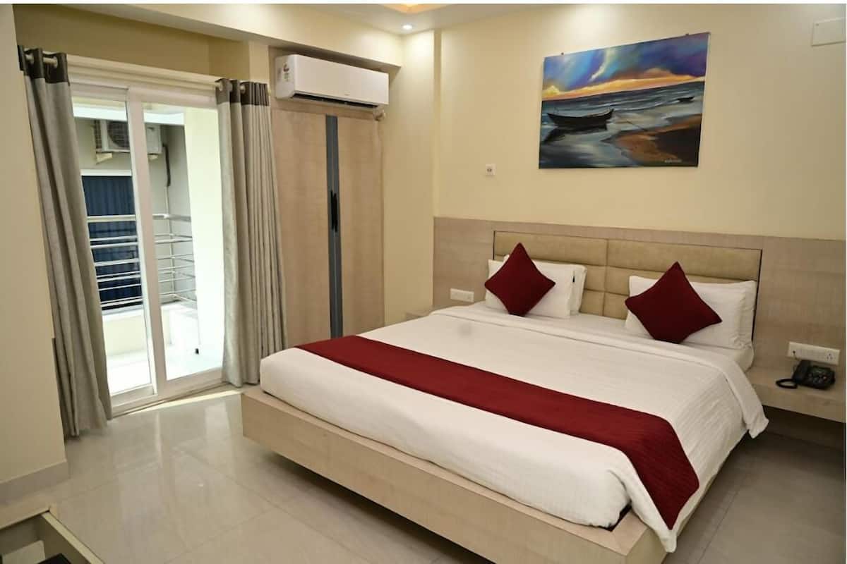 Una habitación de hotel con una cama grande, un cuadro en la pared y un ventanal corredero que da a un balcón.