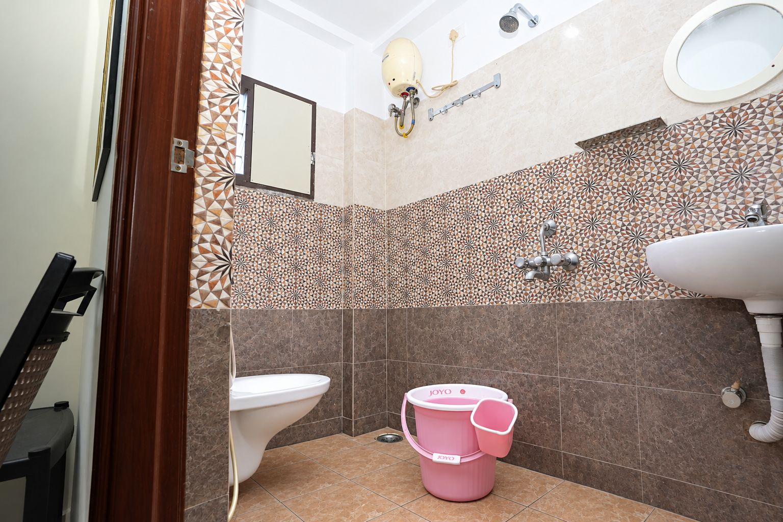 Une salle de bain avec des toilettes, un lavabo, une douche et un seau rose.