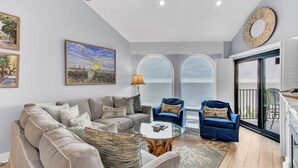 A spacious living room with a large sofa, a coffee table, and two armchairs. There are large windows with a view of the outdoors. - 518 Seascape | Waterfront Views + Community Pool (Isle Of Palms)