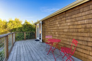 A wooden deck with a metal railing, a door, and two red chairs.