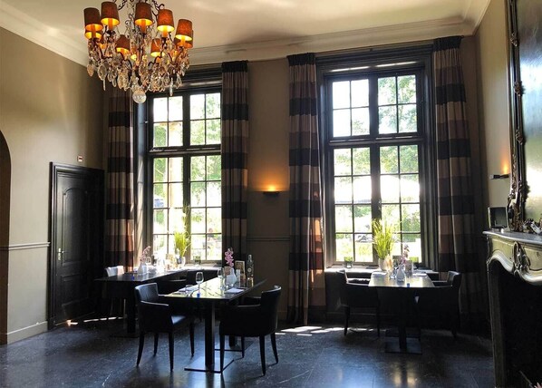 Classic dining area with elegant design, featuring large windows, a chandelier, and a mirror.