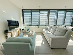 Uma sala de estar moderna com sofá, televisão, uma mesinha e uma janela com persianas.