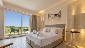 Een ruime slaapkamer met een groot bed, uitzicht op de natuur en een kleine tafel met een lamp.
