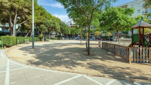 Un parque con árboles, bancos, un área de juegos y un edificio al fondo.