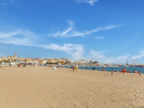 Una playa con cielo despejado, orilla arenosa y un paisaje urbano al fondo.