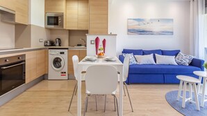 Una cocina moderna con lavadora, una zona de comedor con mesa y sillas, y un sofá azul en la sala de estar.