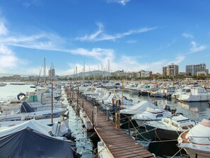 A marina with numerous boats docked along a wooden pier, surrounded by buildings and hills in the background. - Apartment in Palamós near the Beach (Palamos)