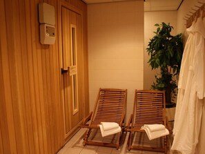 Relax in a serene sauna room with a comfortable seating area and a touch of greenery.