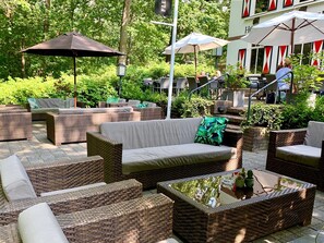 Relax in a serene garden setting surrounded by lush greenery and comfortable wicker furniture.