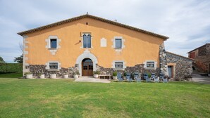 Un edificio de dos pisos con base de piedra y fachada amarilla, que cuenta con una entrada central con puerta de madera y un pequeño porche con plantas en macetas.