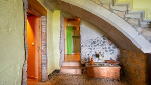 Un estrecho pasillo con una escalera de piedra, un cofre de madera y una cortina verde.