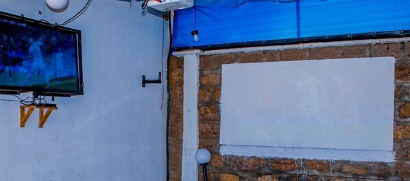 A room with a television mounted on the wall, a blank whiteboard, and a brick wall. - Pearldew Hotel (Kisumu)