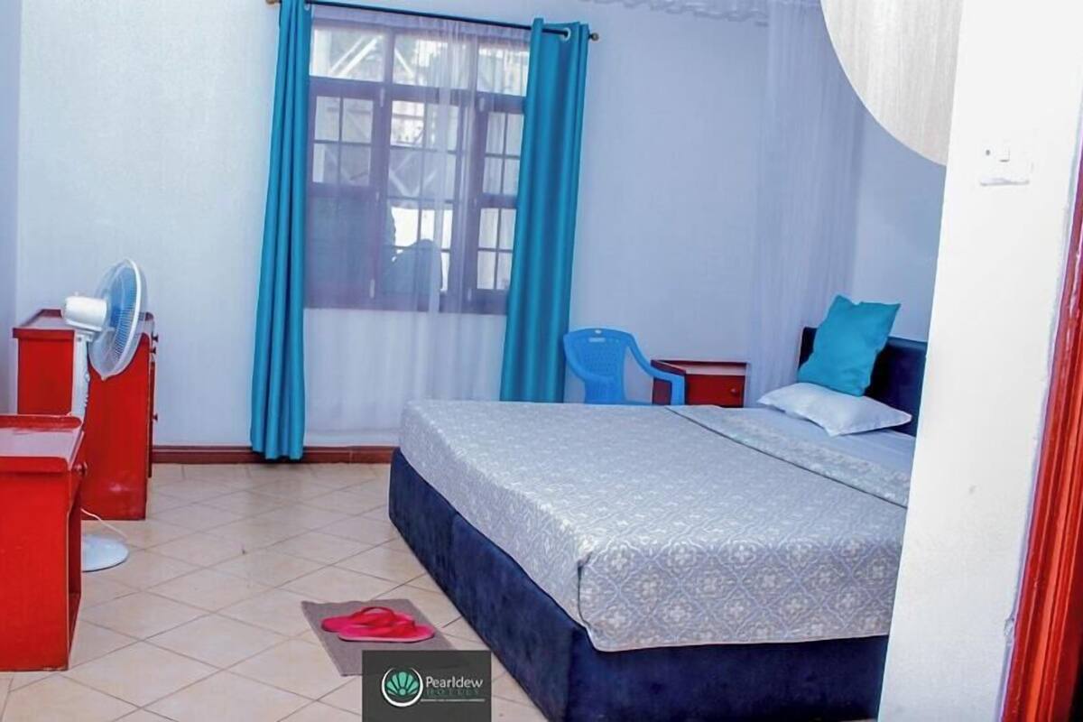 A bedroom with a bed, a desk, a chair, a fan, and a window with curtains.