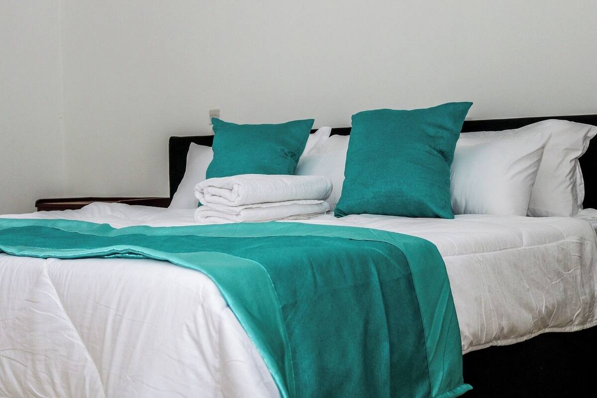 A neatly made bed with white bedding and teal accents, including pillows and a blanket.