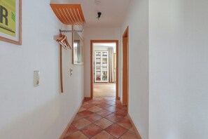 A hallway with a tiled floor, a hanging rack, and a door leading to another room.