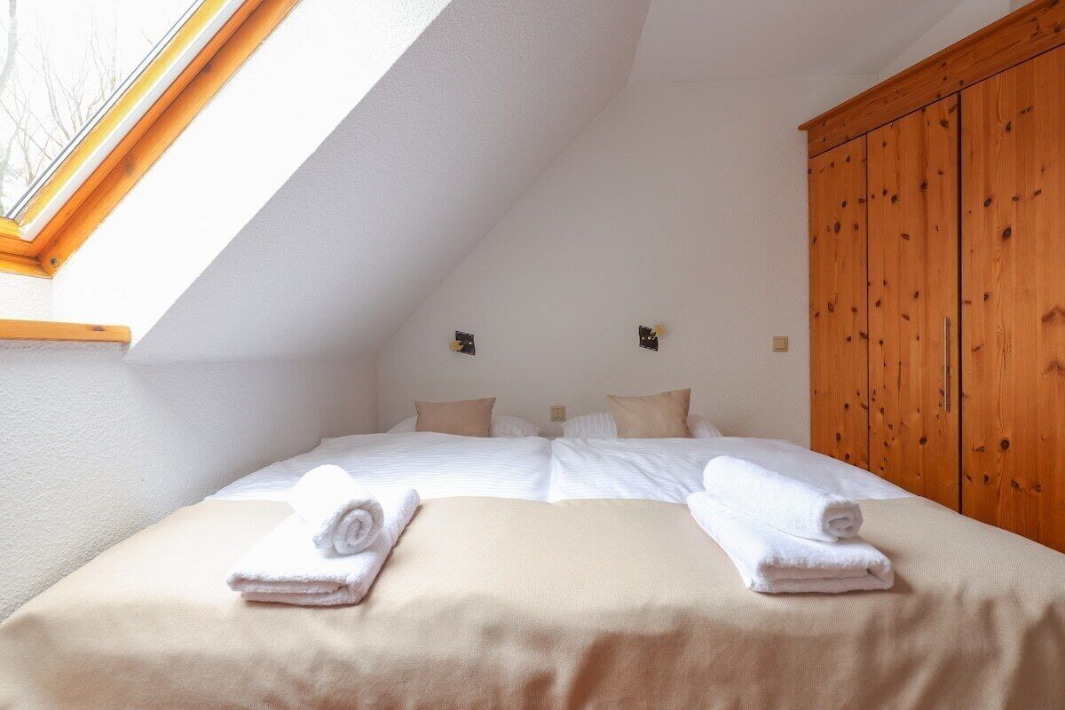 Ein Schlafzimmer mit zwei Betten, einem Oberlicht, einem Holzschrank und einer weißen Wand.