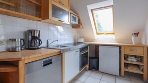 A compact kitchen with a dishwasher, microwave, and coffee maker. - 4 person apartment in green suroundings (Berlin)