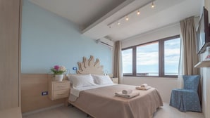 A modern hotel room with a large bed, a bedside table with a lamp, a small chair, and a view of the sea through the window. - Marina Marconi (Bellaria-Igea Marina)