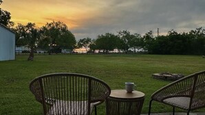 An outdoor patio with wicker chairs and a small table, overlooking a grassy area with trees and a building in the background.