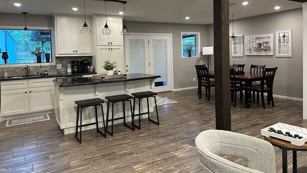 A modern kitchen with white cabinets, a black countertop, and three bar stools.