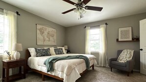 A bedroom with a bed, a nightstand, a chair, a ceiling fan, and a window with curtains.