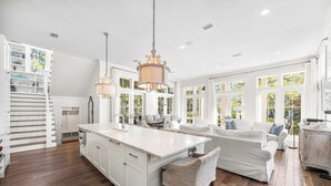 A spacious kitchen with a large island, white cabinetry, and a dining area with white furniture.