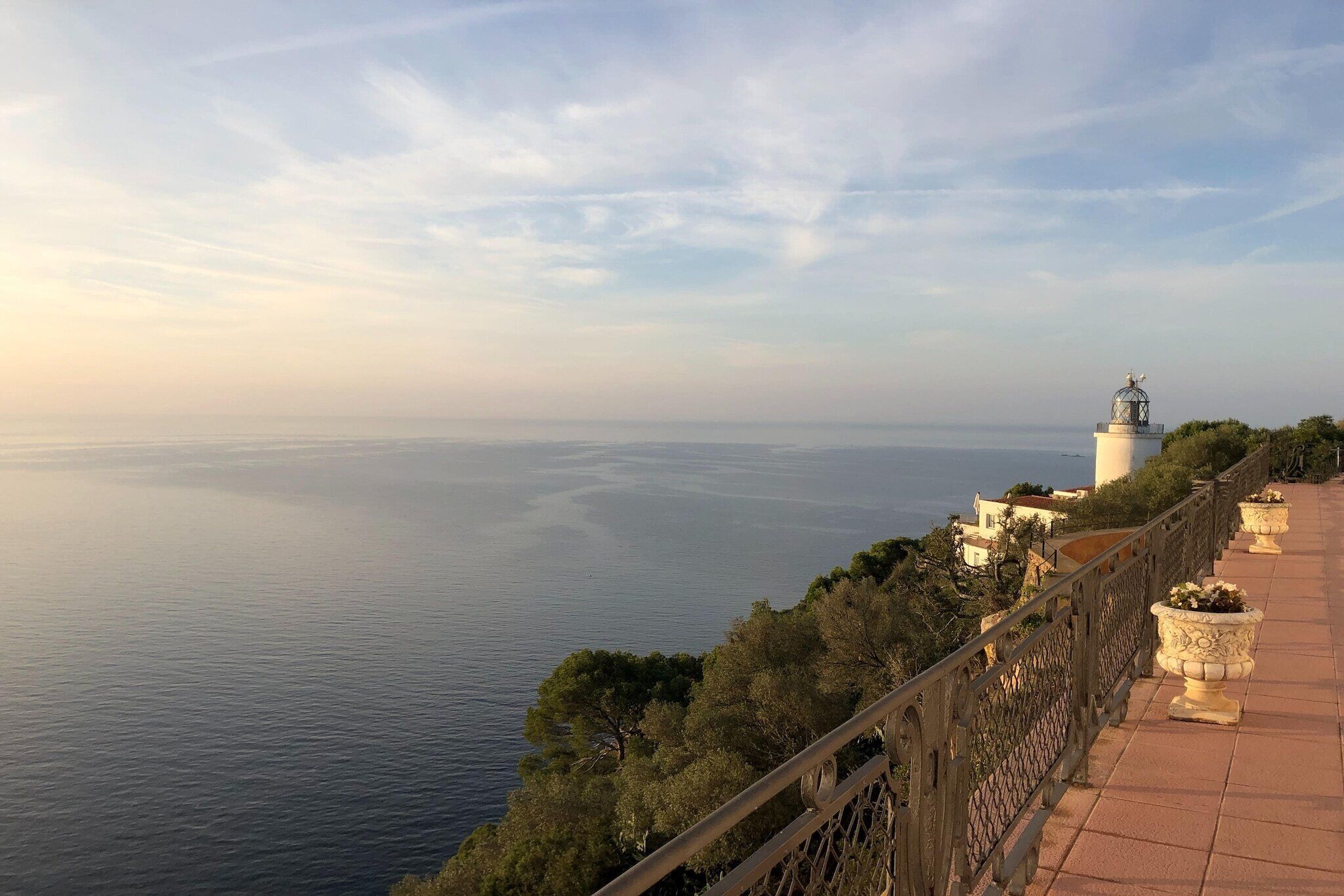 Vista costera con un faro, un sendero pavimentado y una barandilla con vista al mar.
