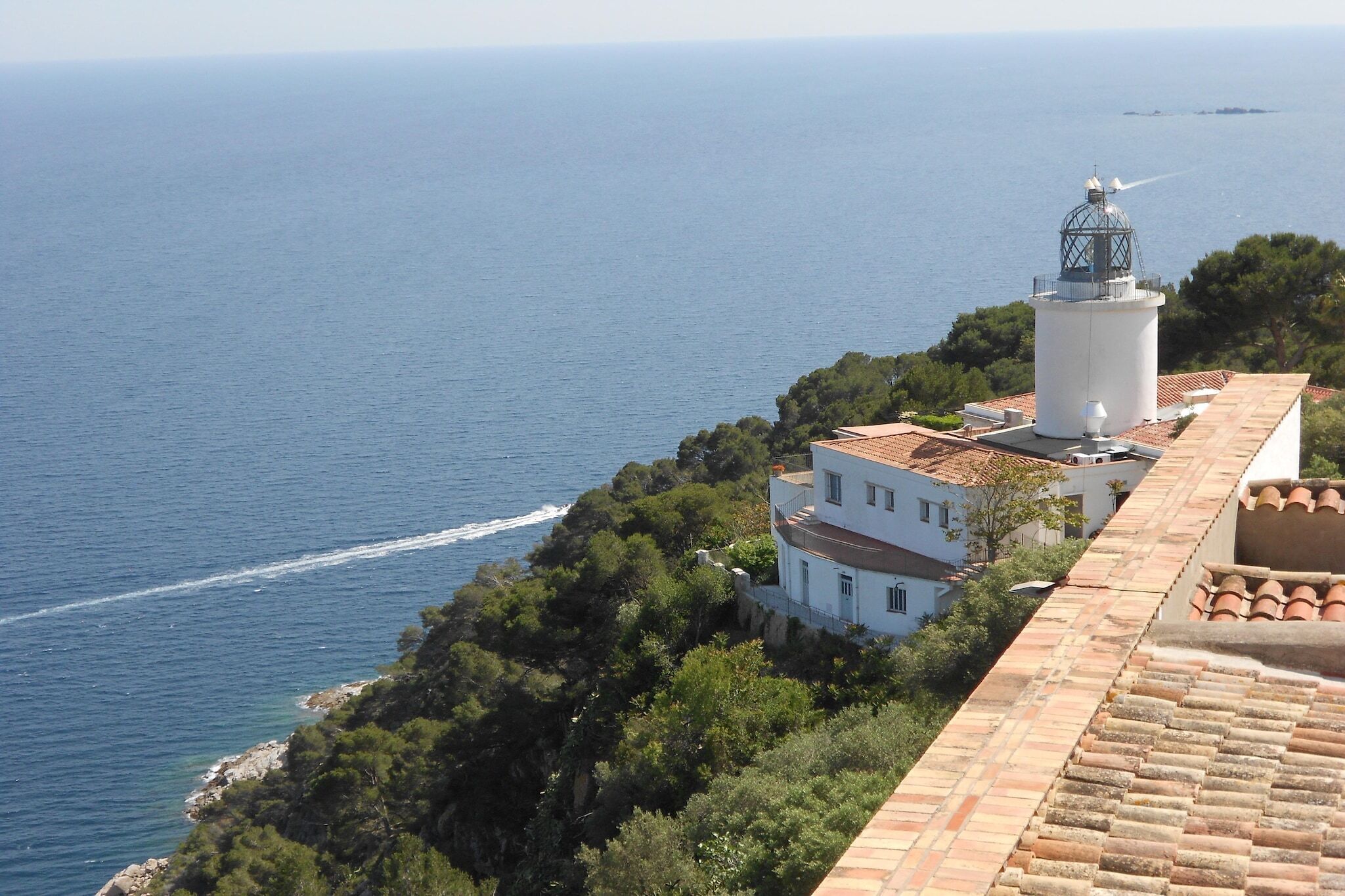 Um edifício costeiro com um farol, rodeado por árvores e com vista para o mar.