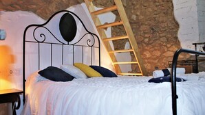 Ein Bett mit Metallkopfteil, einer Holzleiter und einer Steinwand.
